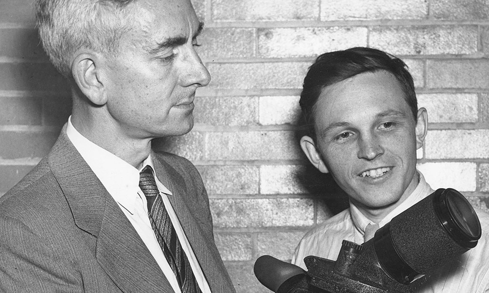 historic image of two men holding an optica device called an Icaroscope, which looks like a large, camera lens