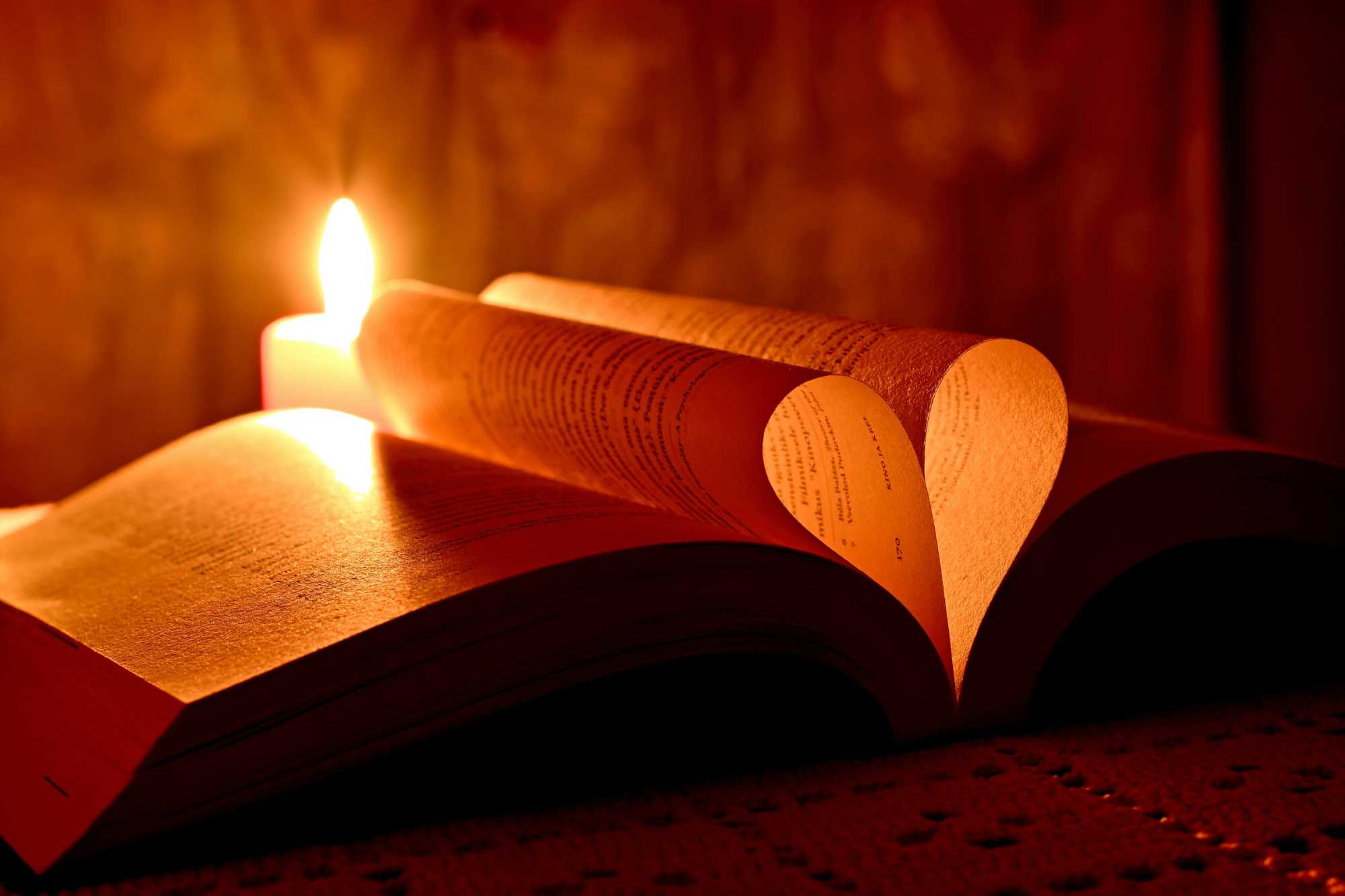 Opened book with two pages forming a heart while a candle glows in the background.
