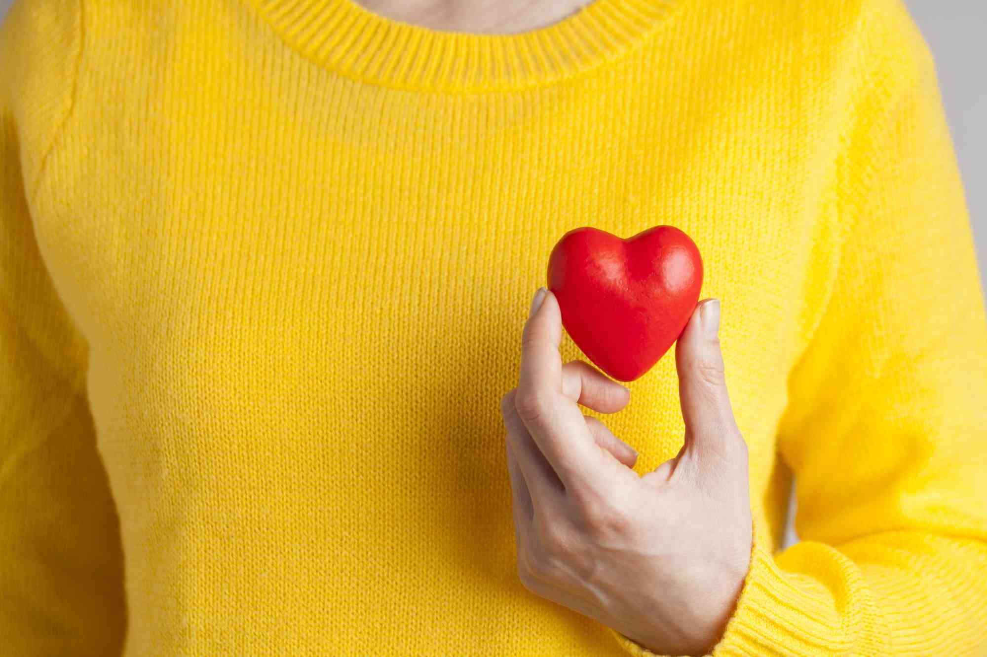 Hand of a person holding a plastic heart while wearing a bright yellow sweater.