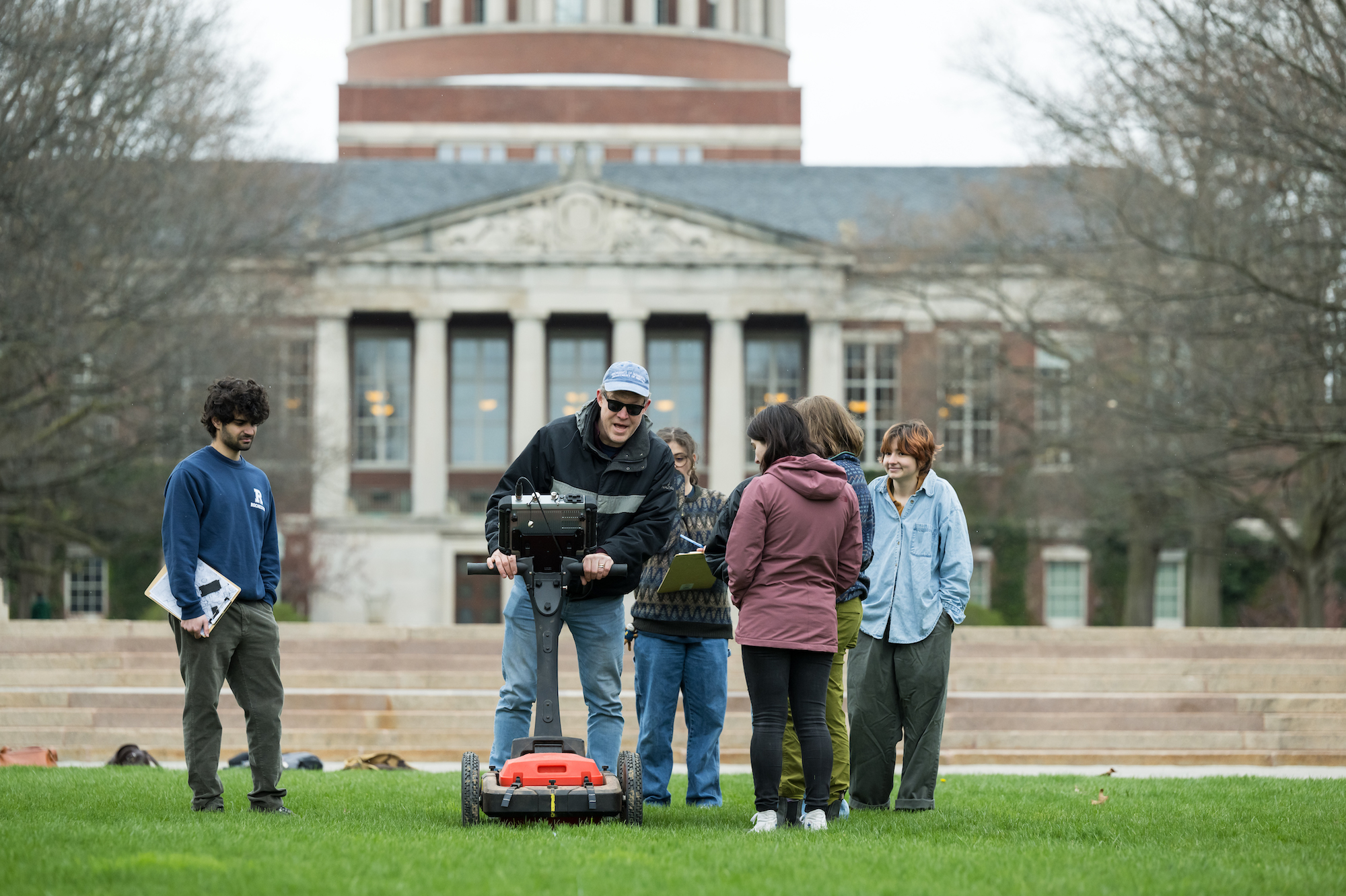Professor and a group of students out on a grassy quad with survey equipment