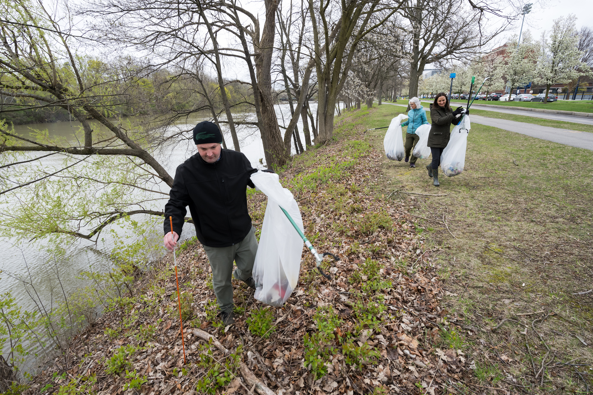 Three people pick up garbage along a riverbank