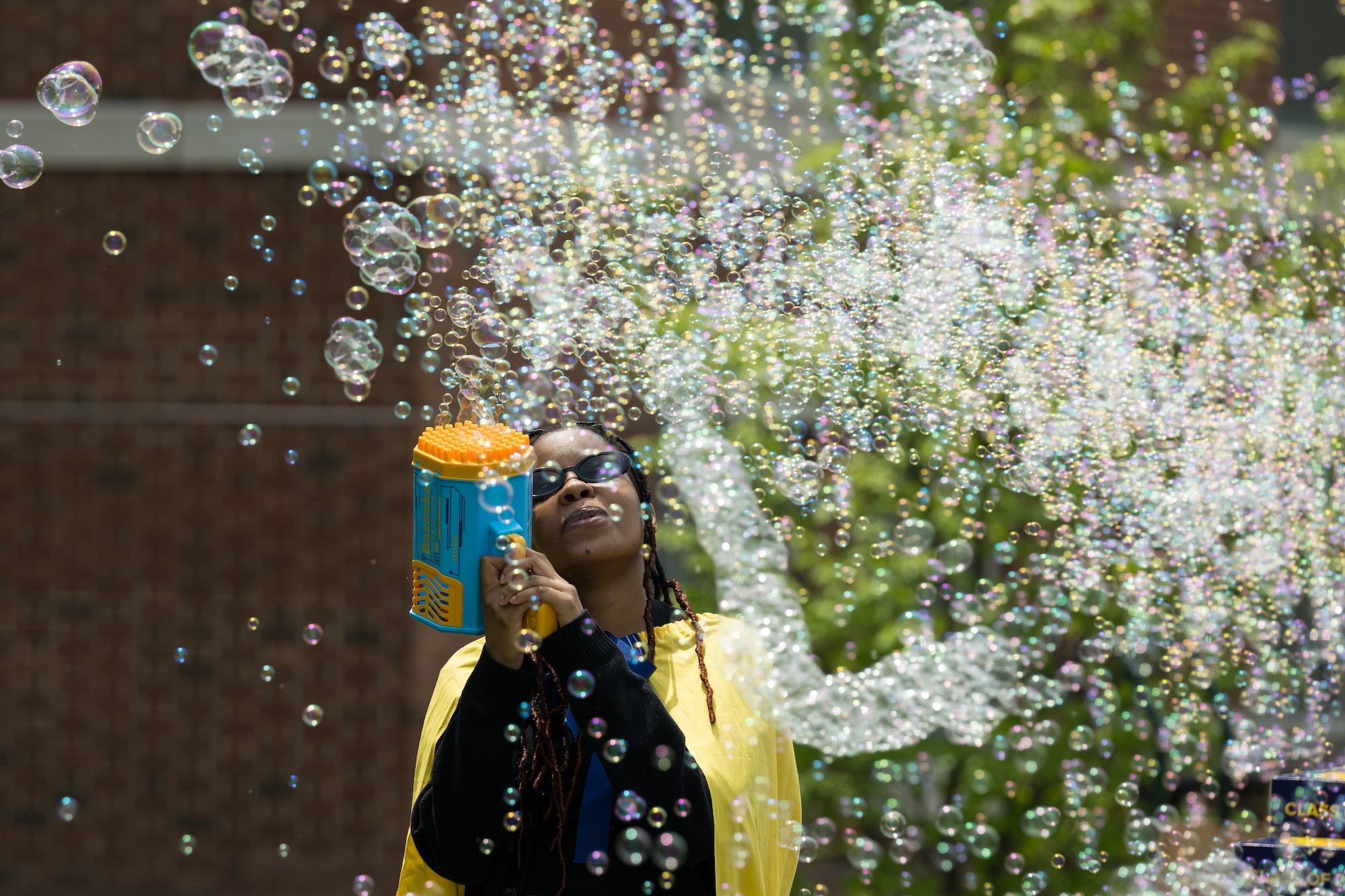 University of Rochester student in sunglasses blowing bubbles through a bubble gun