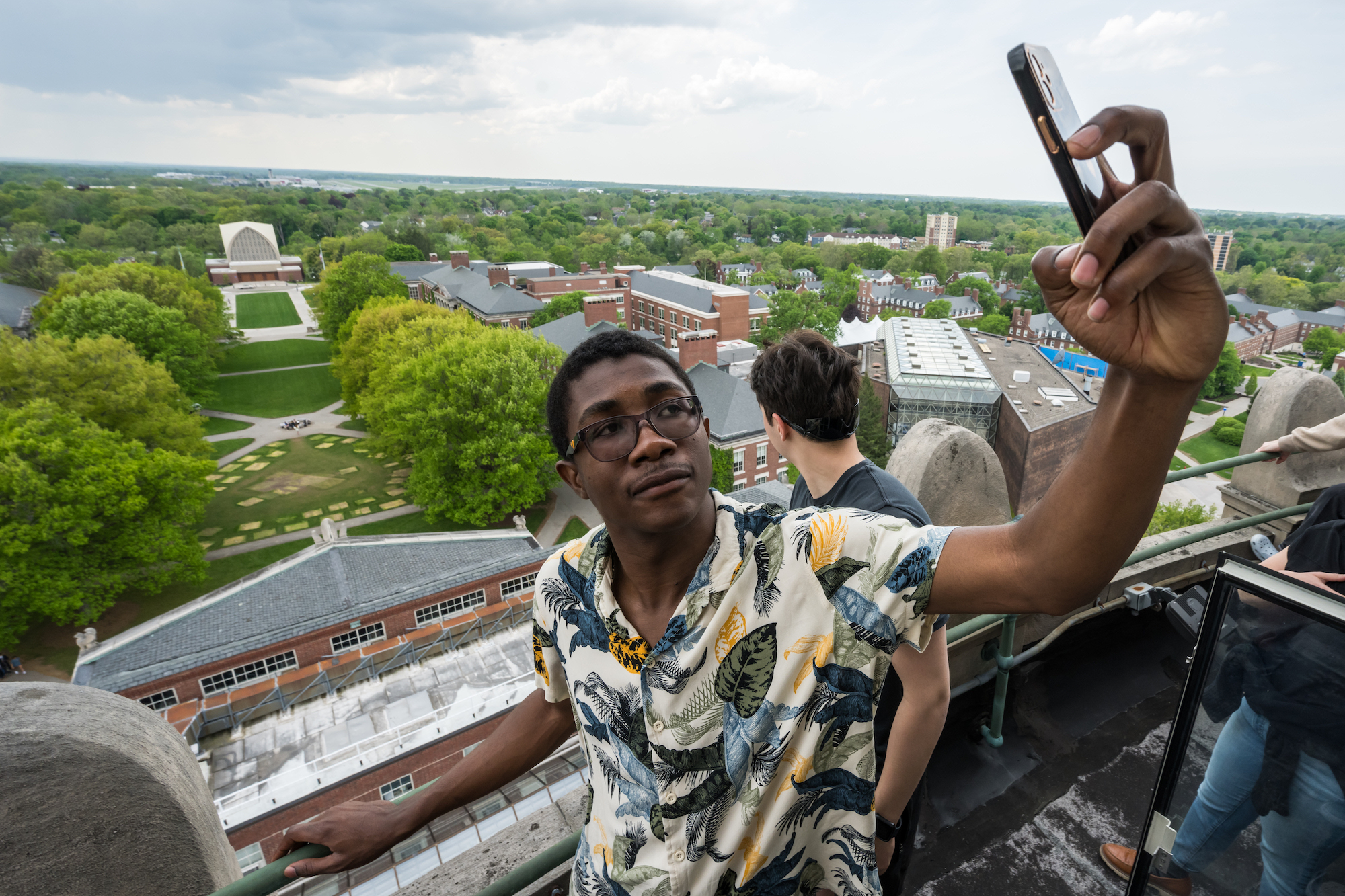 A student atop the library tower takes a selfie with the University of Rochester campus below