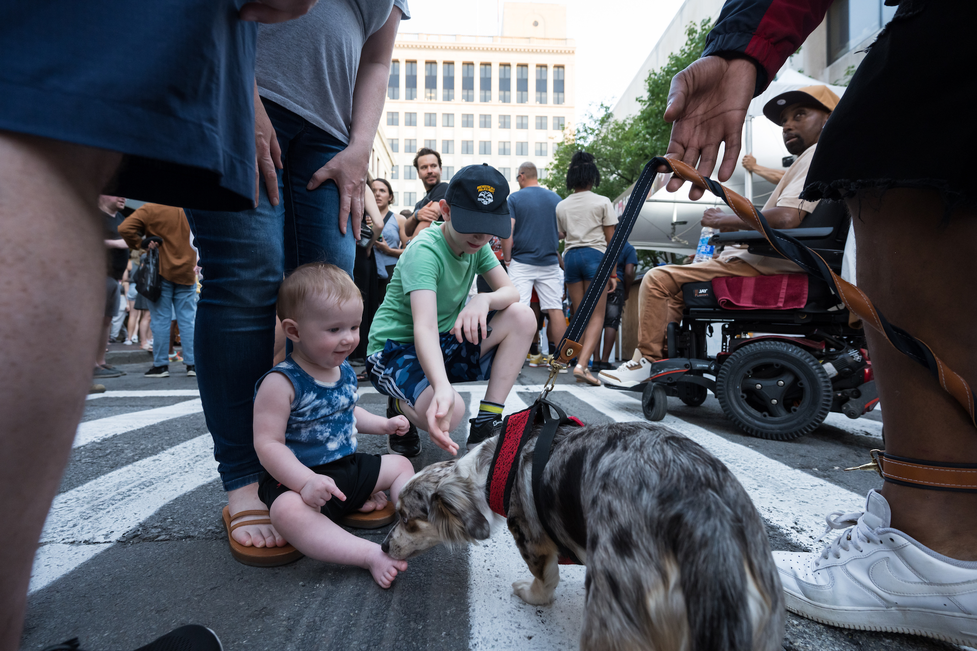 A baby and a small child are pictured with a tiny dog outside among a crowd of people