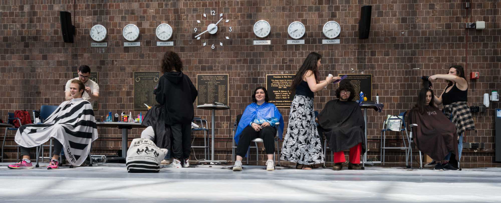 Wide angle shot of four college students getting their haircut by four ClipDart hairstylists in Wilson Commons.