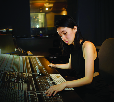 Ching-Shan Chang in black sleeveless shirt seated at synthesizer in recording studio.