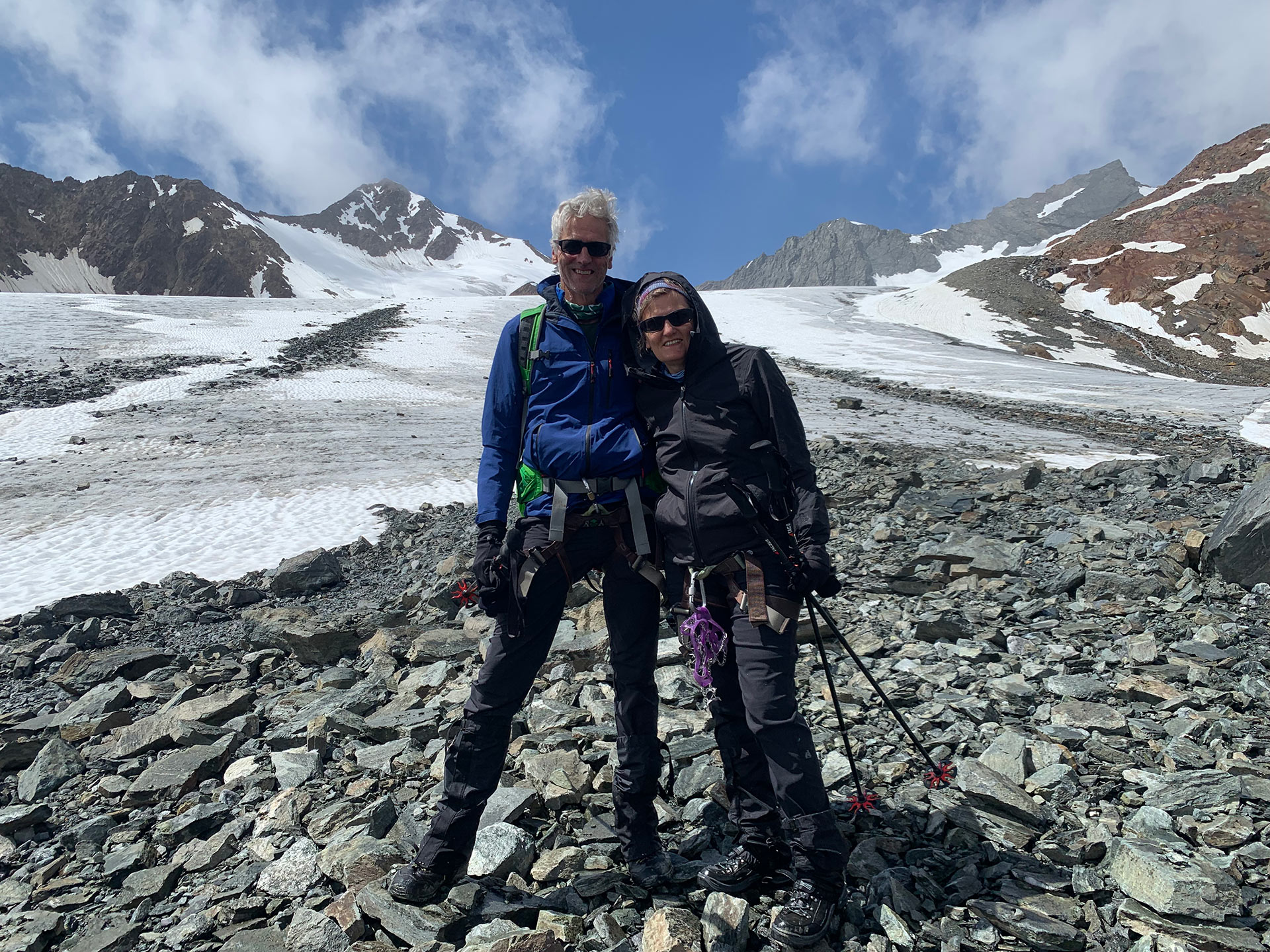 Two hikers in mountaineering gear pose and smile, with a glacier in the background.