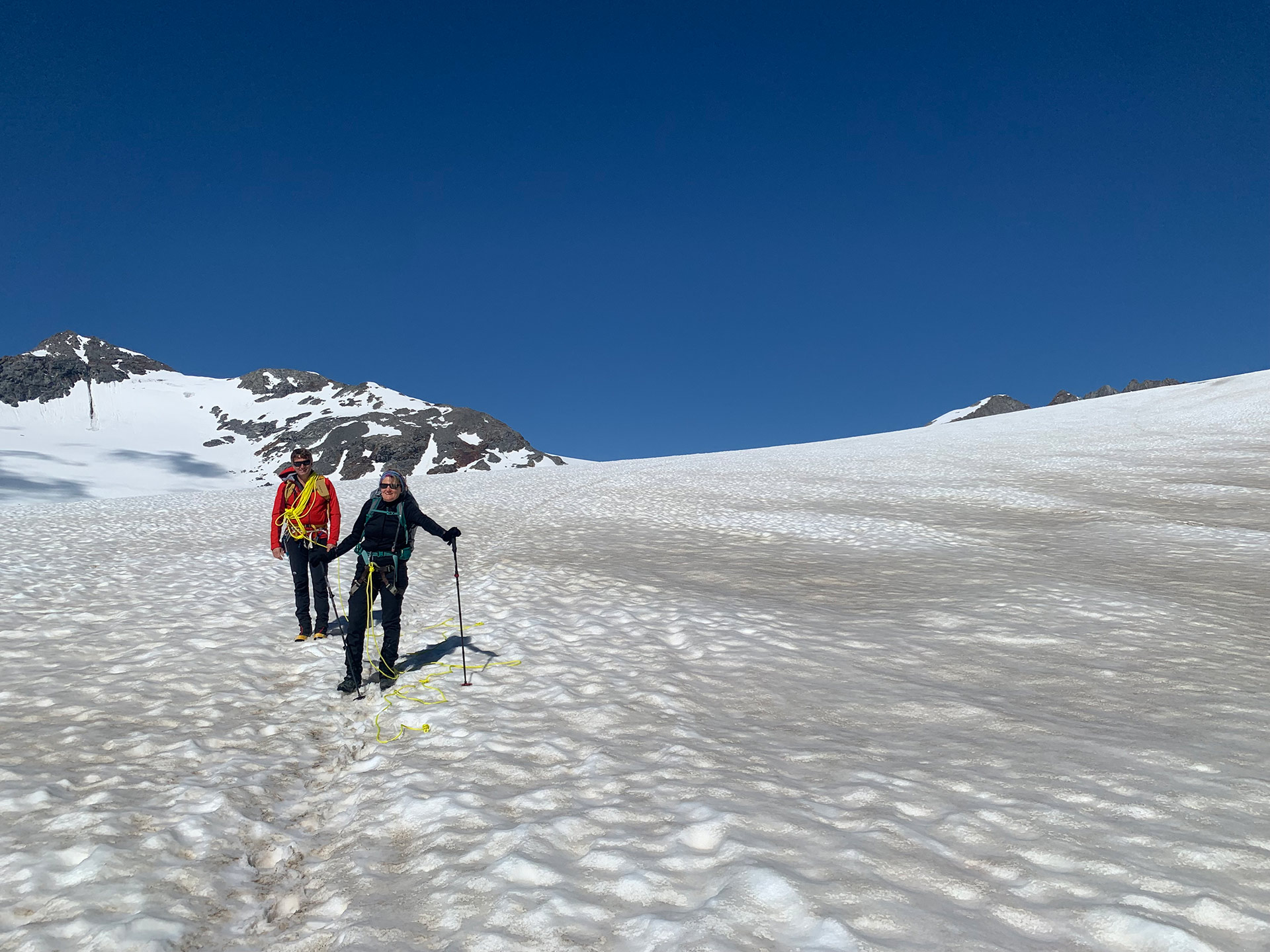 Two hikers in climbing gear pose for a photo on a glacier.