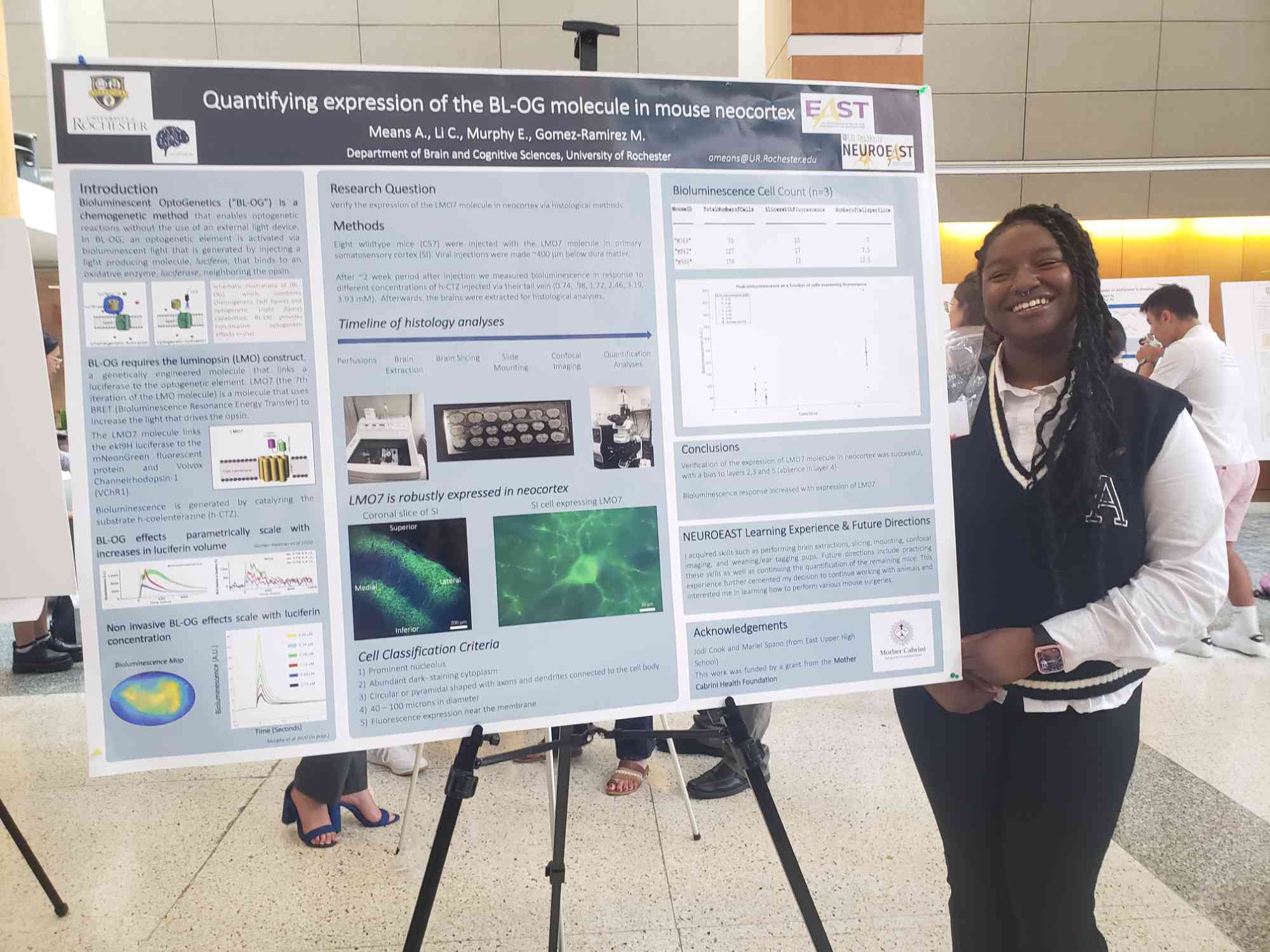 Aniya Means smiles while standing next to her poster showing research she conducted on bioluminescent 