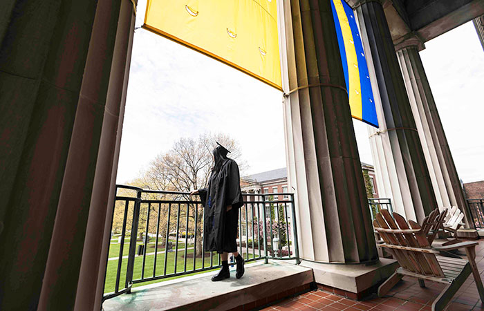 A candid photo of a senior in a cap and gown looking out at the Eastman Quad from Rush Rhees library.