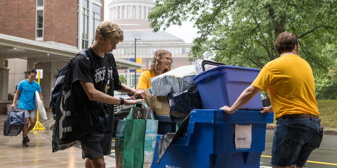 Students transport belongings in a large rolling bin on move-in day
