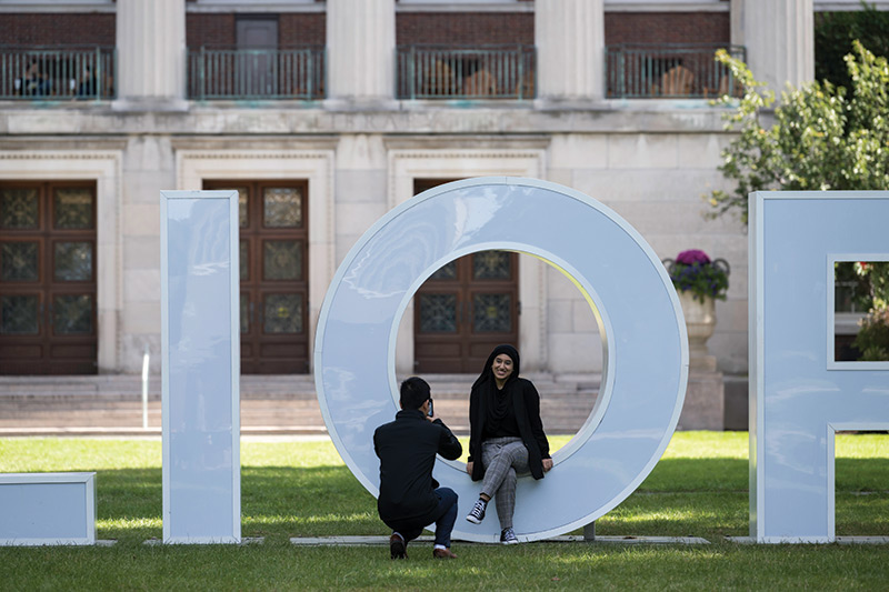 photo of University of Rochester students taking photos in the letter O of Meliora in set of letters set up on a campus quad