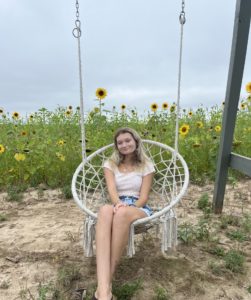 Summer Koltay sitting in a swing in front of a sunflower field