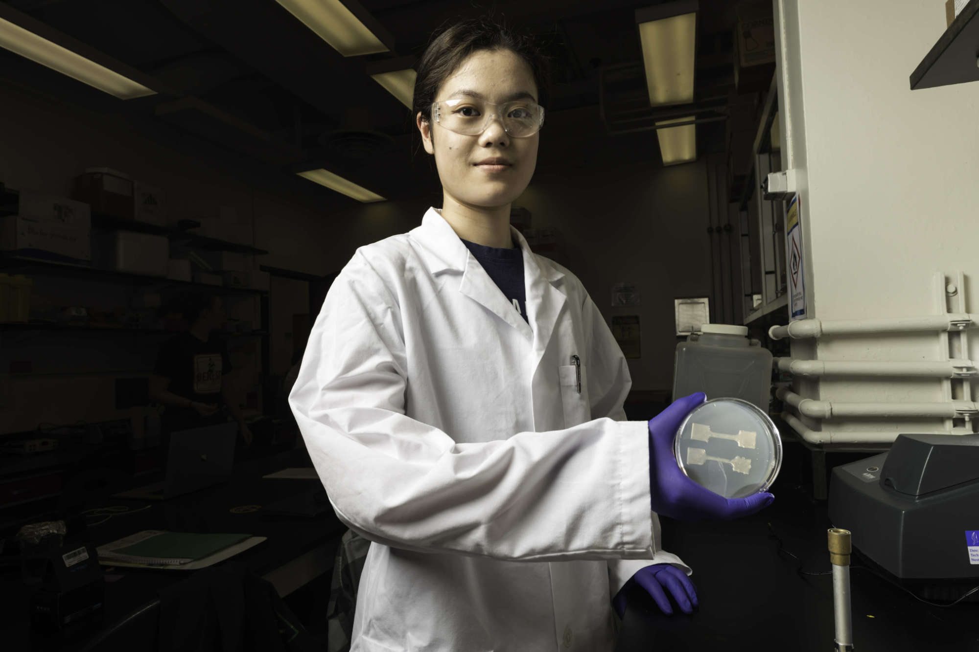 Student in a lab coat holds a dish plant-derived material printed on media and made with 3d bioprinting.