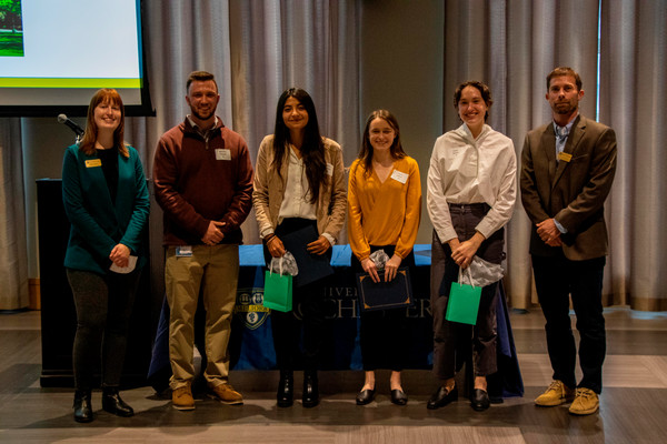 Four students and a professor in a group smiling at the camera while the students hold their certificates.