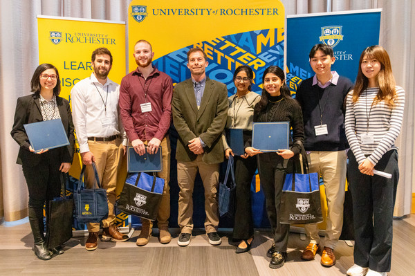 Seven students and a professor in a group smiling at the camera while the students hold their certificates.