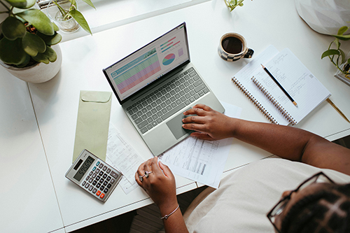 A person shown from above working on a laptop with a calculator and cup of coffee.