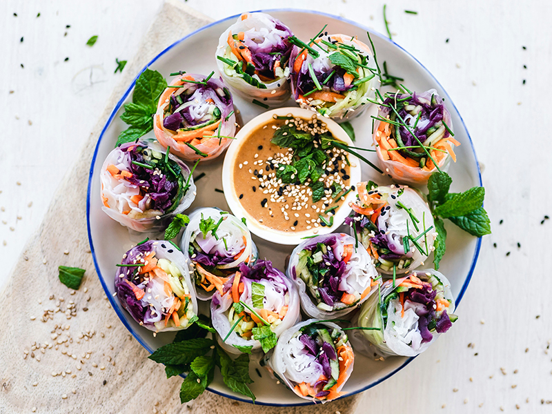 Colorful spring rolls as seen from above standing on end on a white plate with dipping sauce in the center.