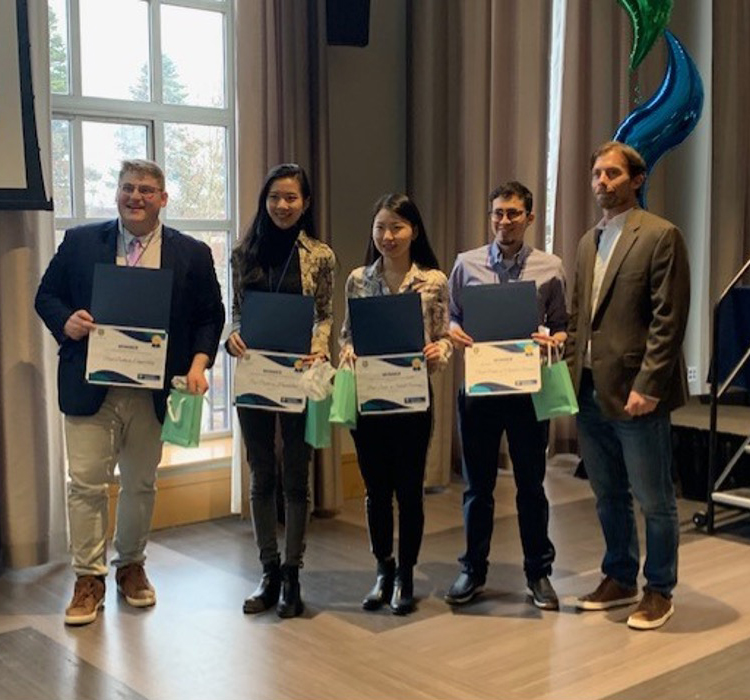 Four students and a professor in a group smiling at the camera while the students hold their certificates.