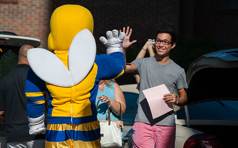 Photo of a student high-fiving Rocky while holding their Residential Life check-in materials