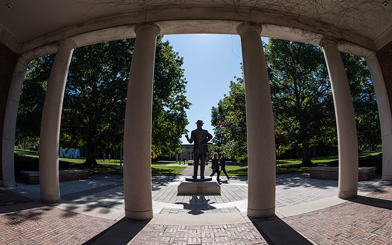 Photo looking out onto Eastman Quad from behind the pillars and the George Eastman statue