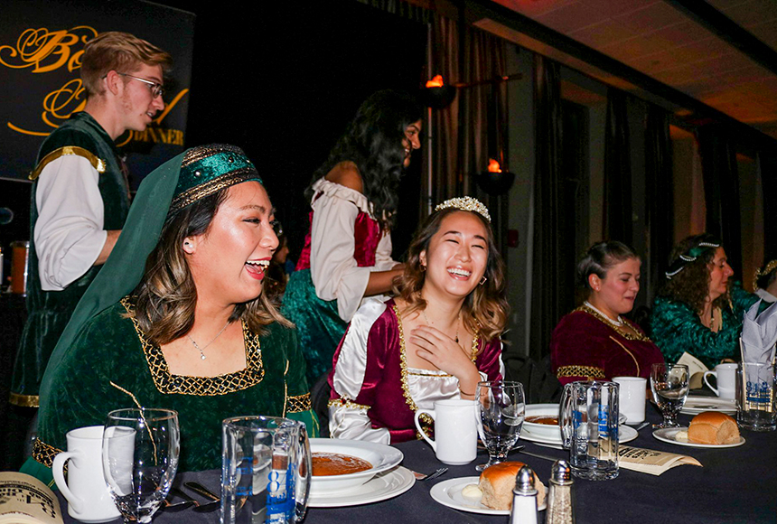 Photo of students and staff dressed in medieval clothing seated at a table with food in front of them