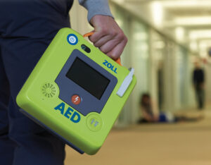 Man carrying a lime green Zoll Automated External Defibrillator (AED) 3 device featuring a touchscreen display.