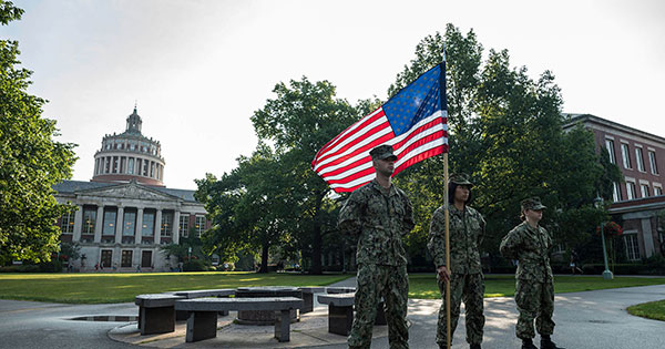 Building in view with three navy soldiers standing in front of a fountain holding up a USA flag