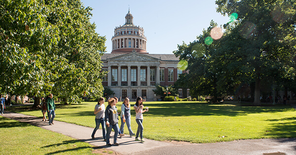 Students between classes in the Eastman Quad on the University of Rochester's River Campus. Rush Rhees Library can be seen in the background.