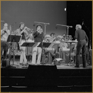 black and white image of orchestra on stage, playing trumpets