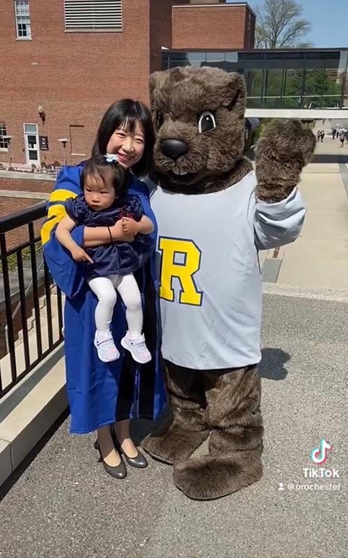 Groundboi poses with graduate and child on campus