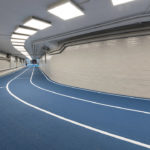 blue running track with three lanes surrounded by white cinderblock wall