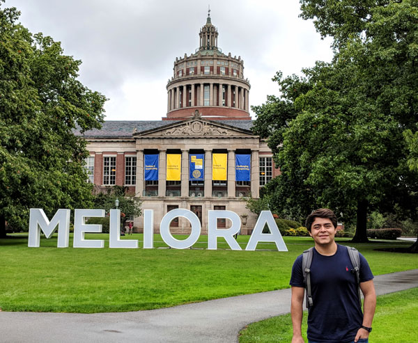 Obed Badillo Moreno ’19 standing in front of rush rhees with the large meliora letters in the quad