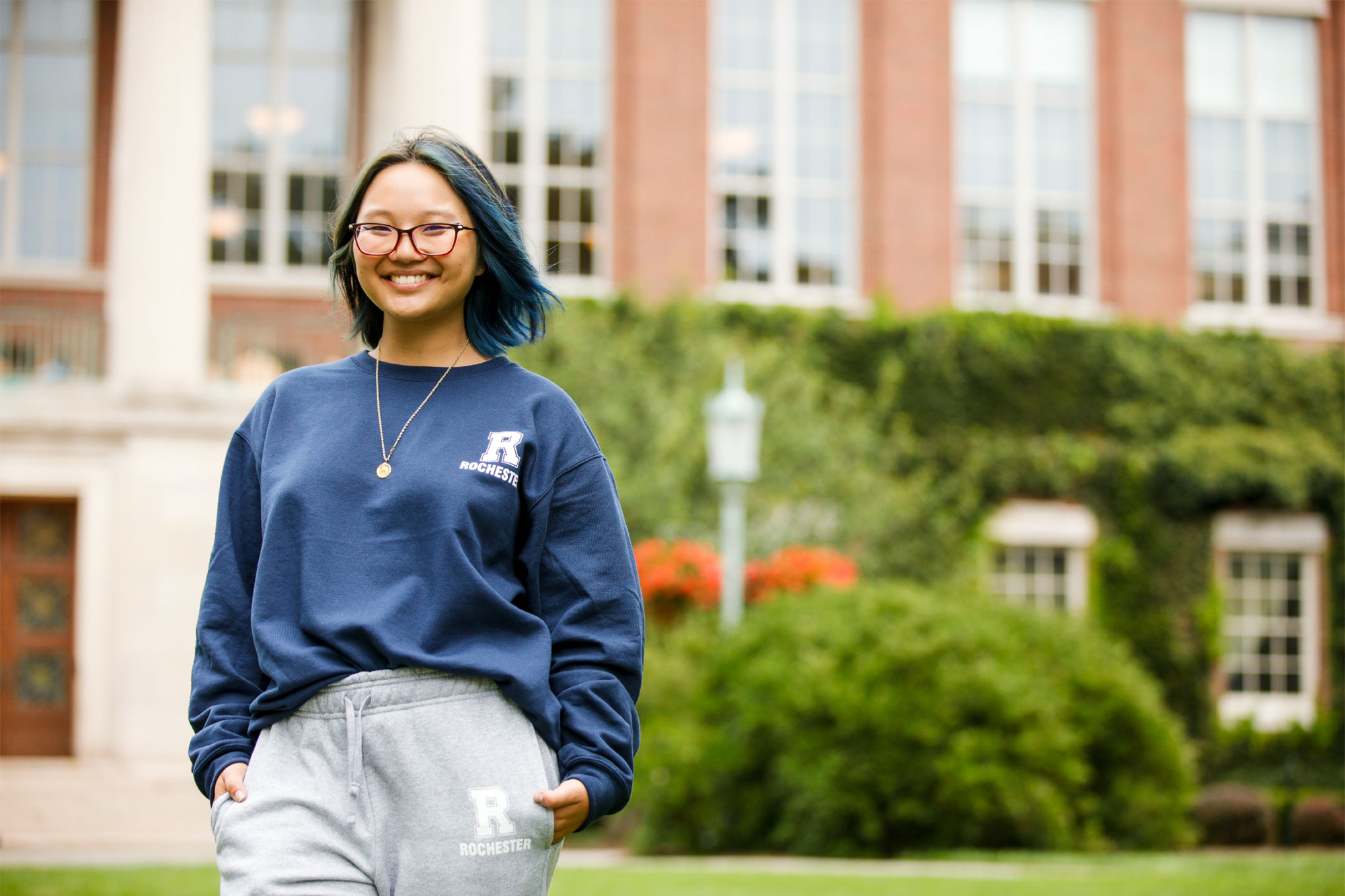 student stands in front of Rush Rhees wearing sweatshirt and sweatpants