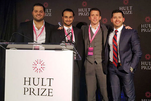 4 men behind a lecturn posing and smiling for the camera