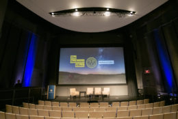 large screen on stage with the rochester effect graphic and empty auditorium