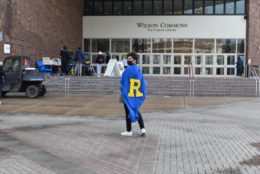 the back of a male student wearing blue cape and a yellow R in front of wilson commons stairs