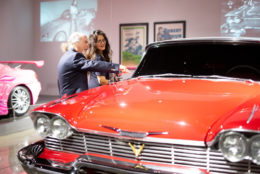 man pointing at vintage bright red car next to woman