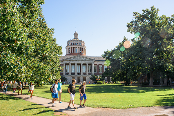 Students walk across Eastman Quad in front of Rush Rhees Library on a sunny day.