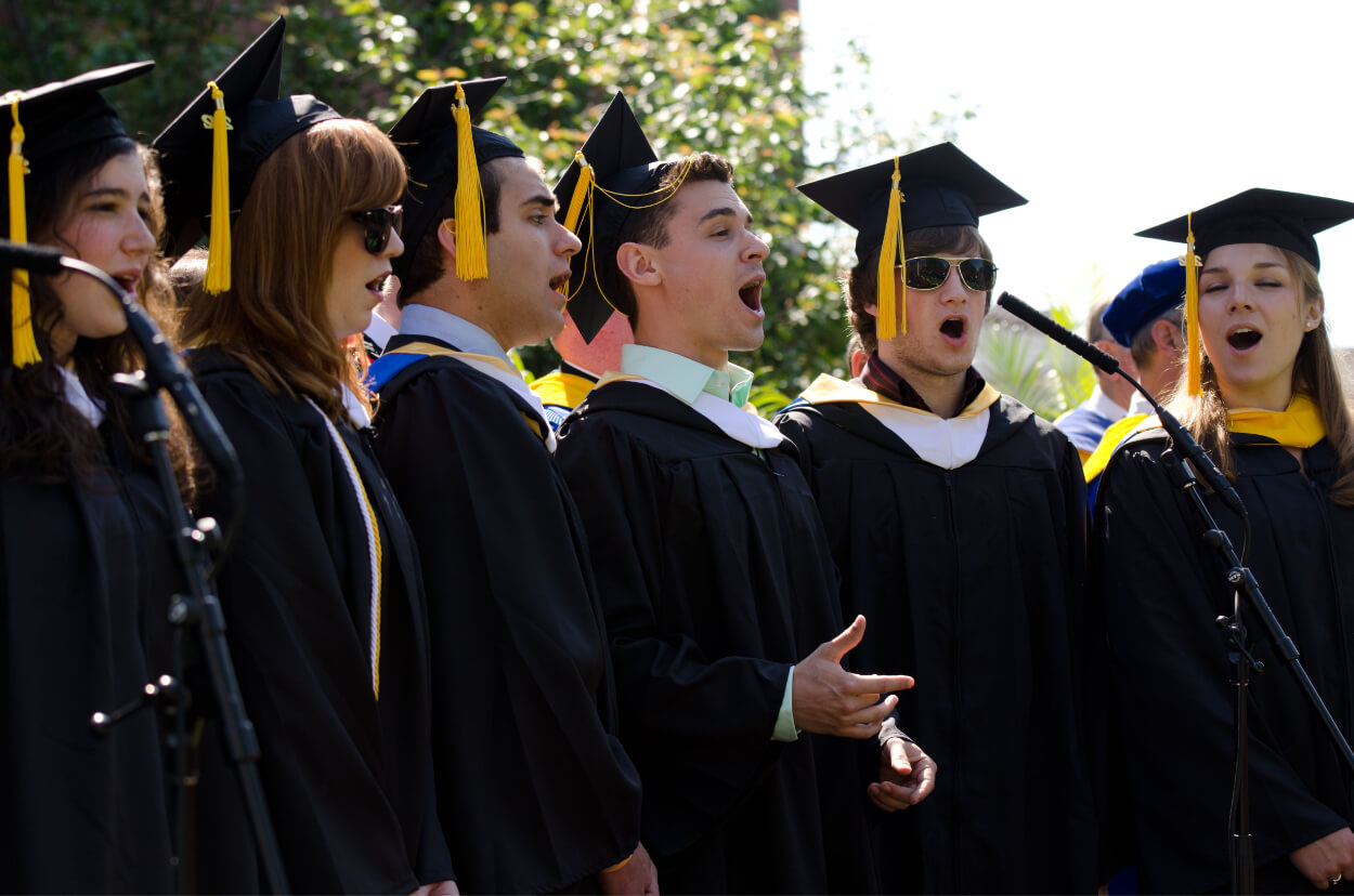 University of Rochester graduates in hat and gown singing the alma-mater at commencement