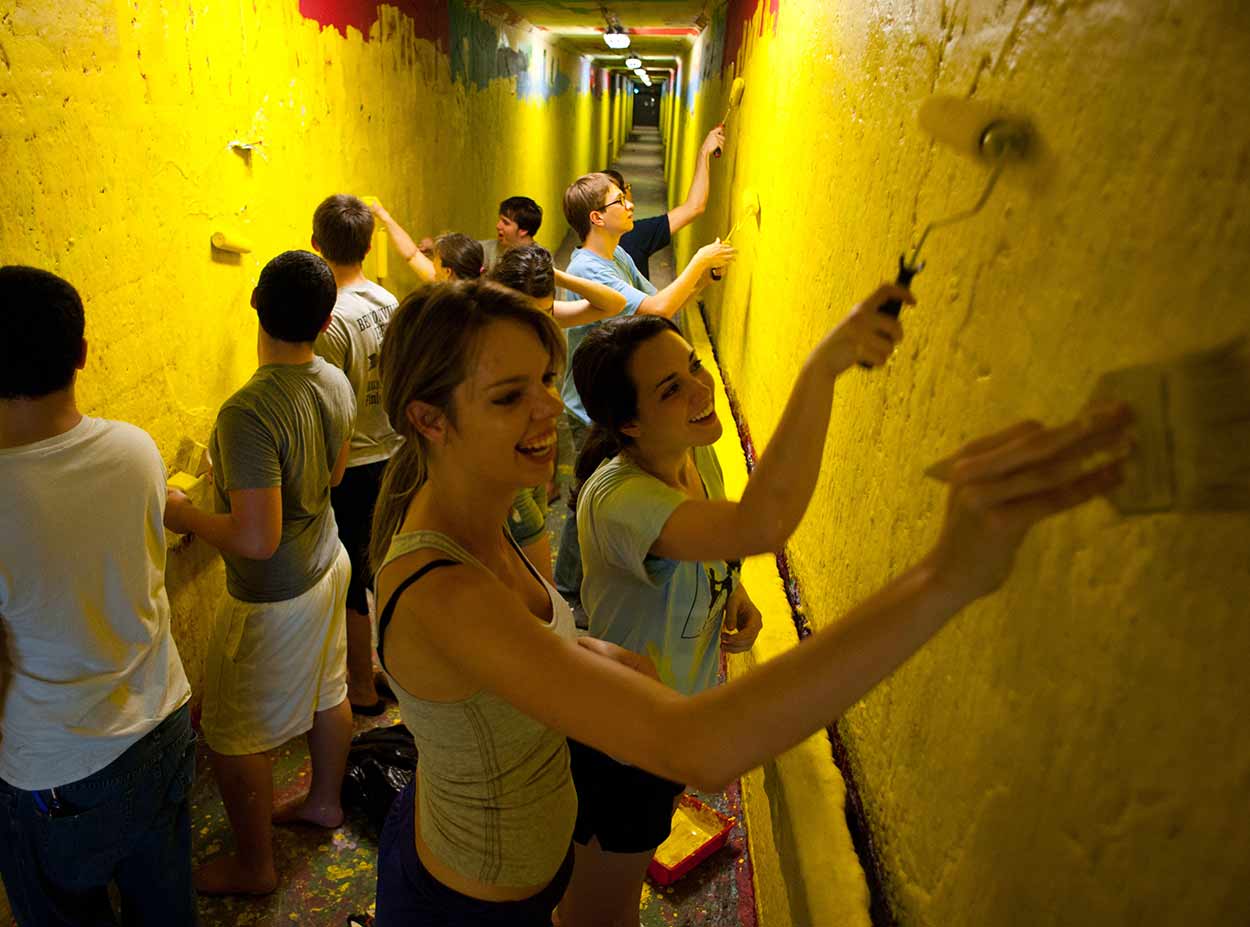 Students painting over graffiti walls in tunnels at University of Rochester