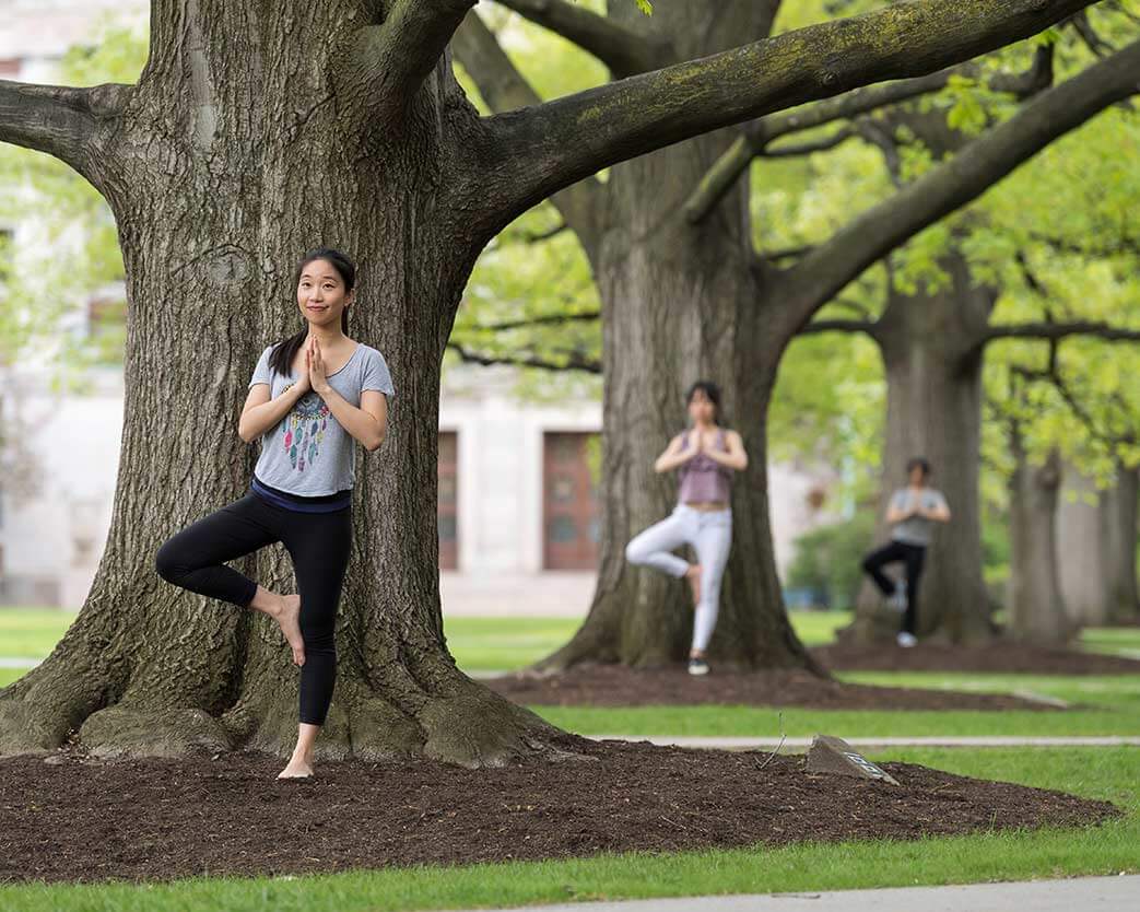 Three students standing in front of three trees doing yoga tree pose at University of Rochester