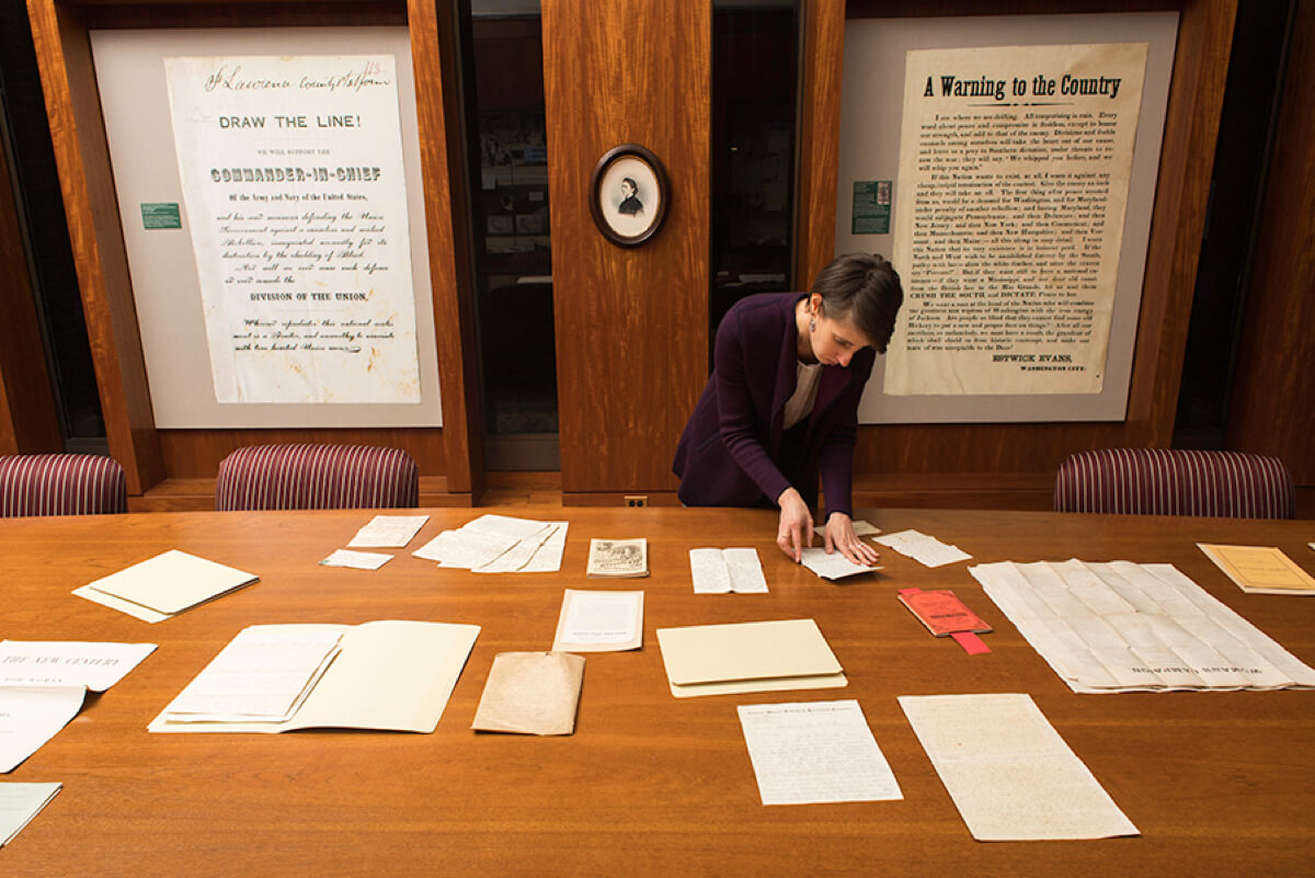 librarian at a large table arranges letters in front of posters about women's suffrage. 