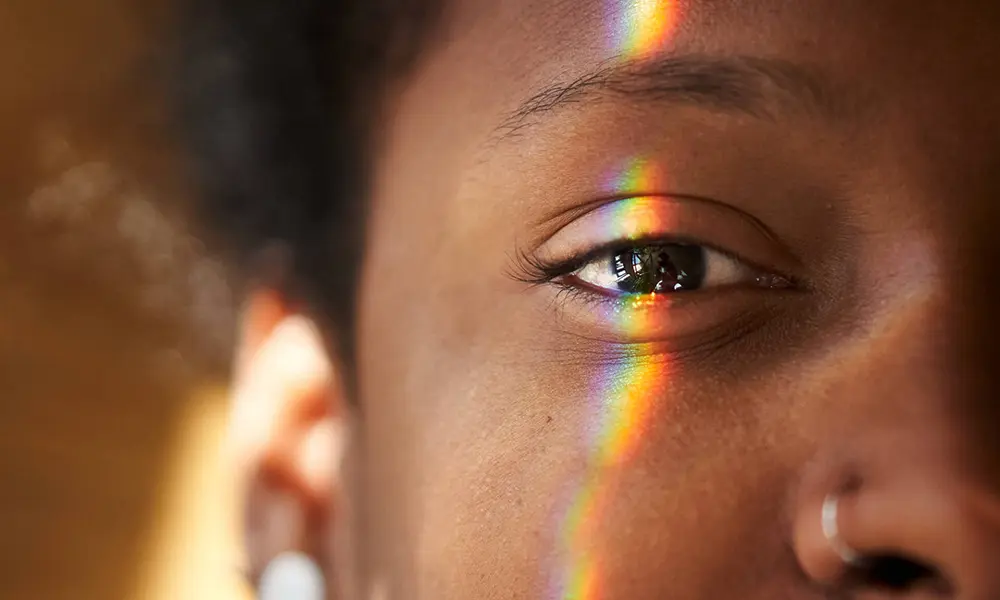 Close-up of a Black person's eye with a multicolored light falling on it to illustrate how retinal ganglion cells function.