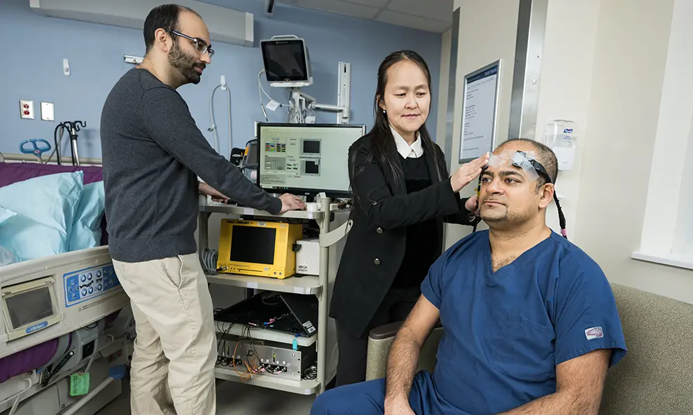 Imad Khan, M.D., assistant professor of neurology and neurosurgery, models a device prototype.