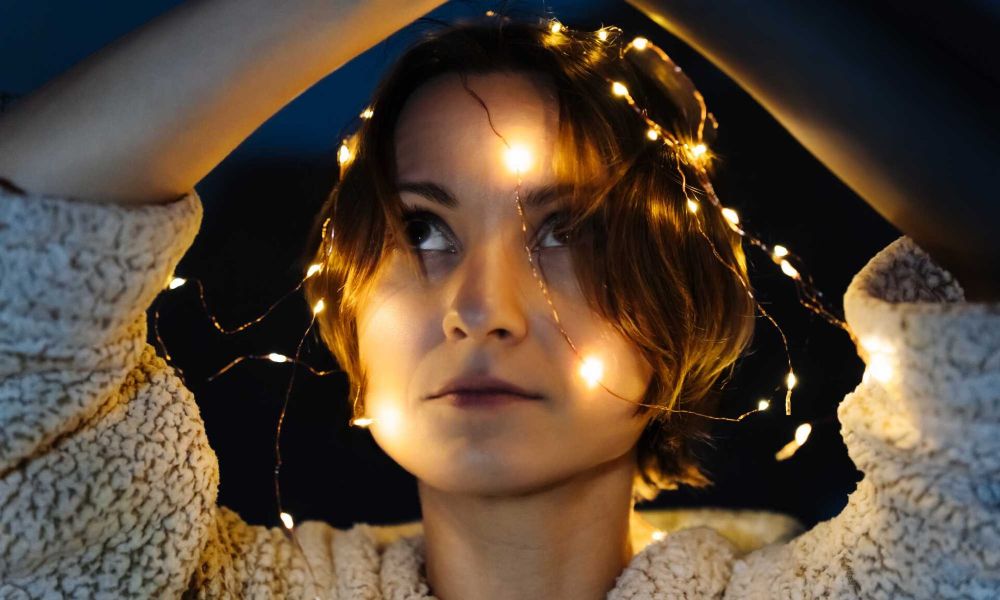 Close-up of a person with fairy lights around their head, wearing a fluffy sweater.