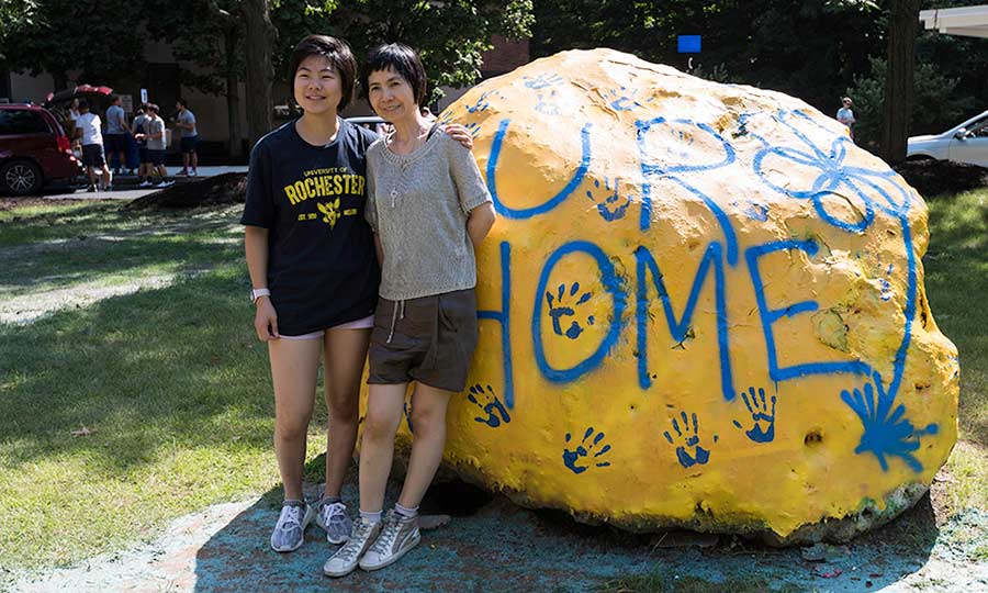 mother and daughter standing outside of residence hall in front of a large rock painted to read UR HOME
