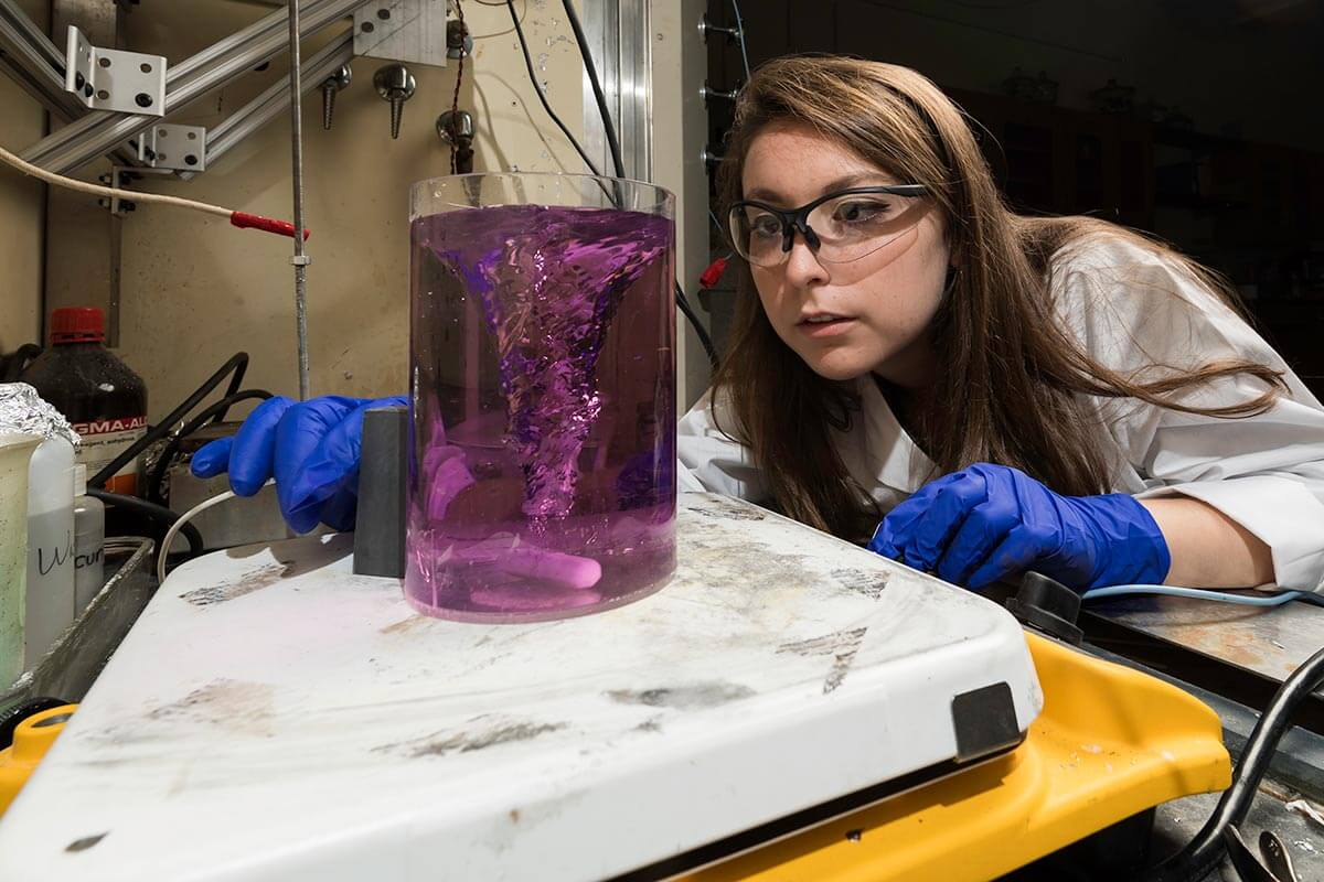 Student researcher looking at beaker of purple liquid in lab at University of Rochester 