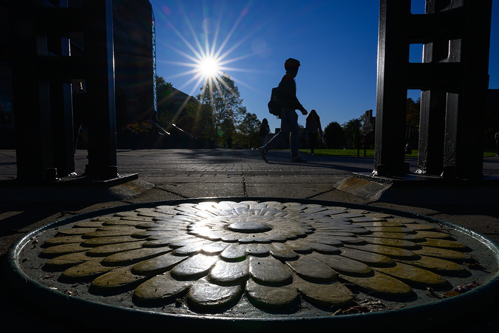A ground-level view of a student walking across campus in silhouette.