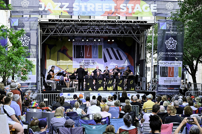 A Jazz band plays on a stage during the Jazz Festival as viewers listen from the street.